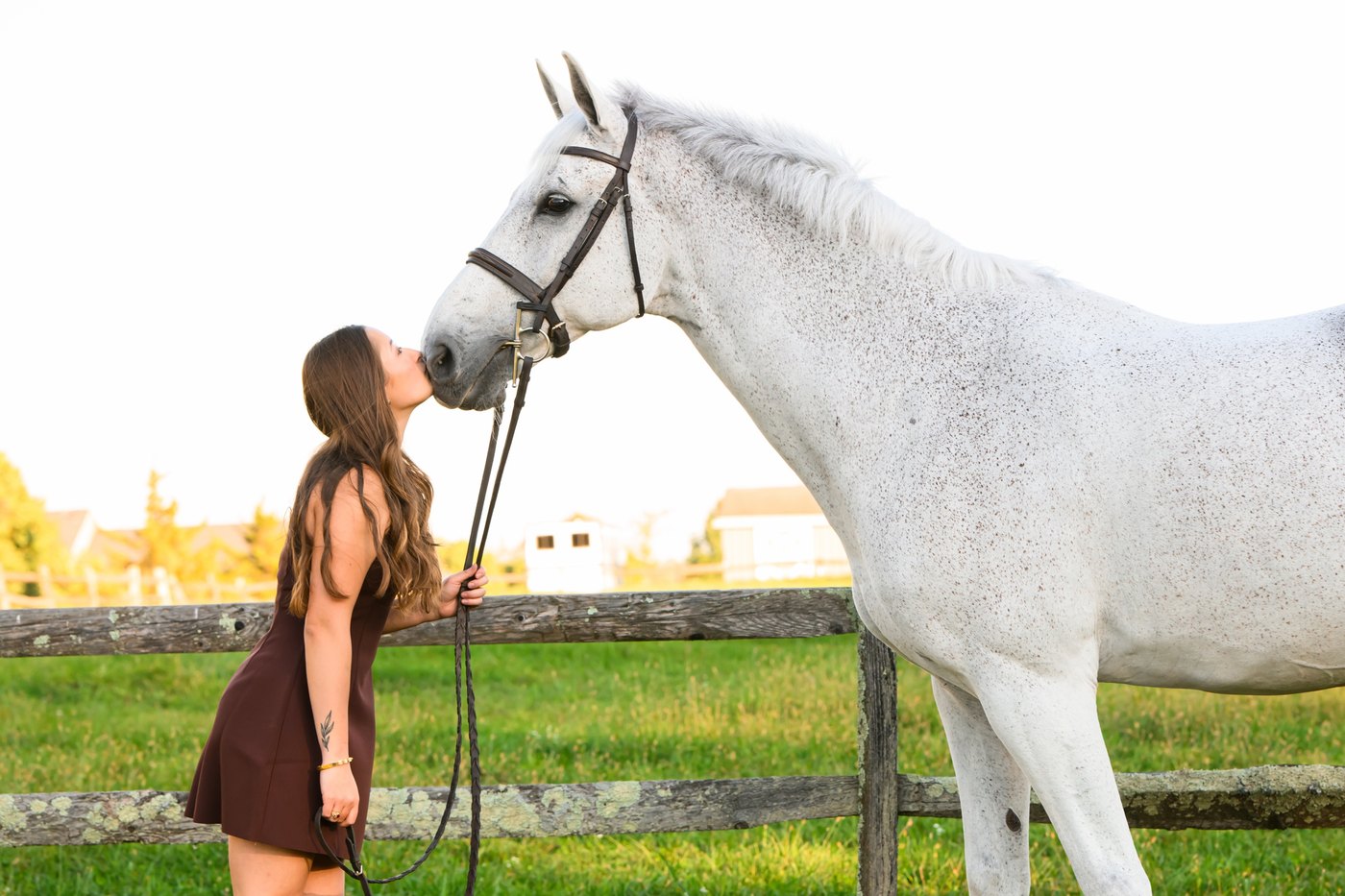 A rider resting against her grey horse in the autumn light