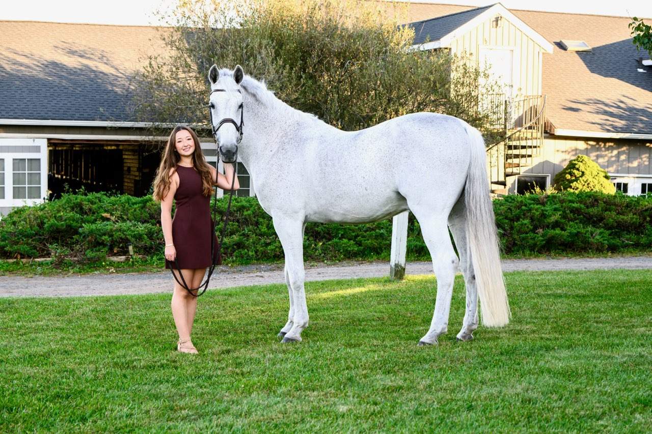 A rider with her grey horse outside the barn