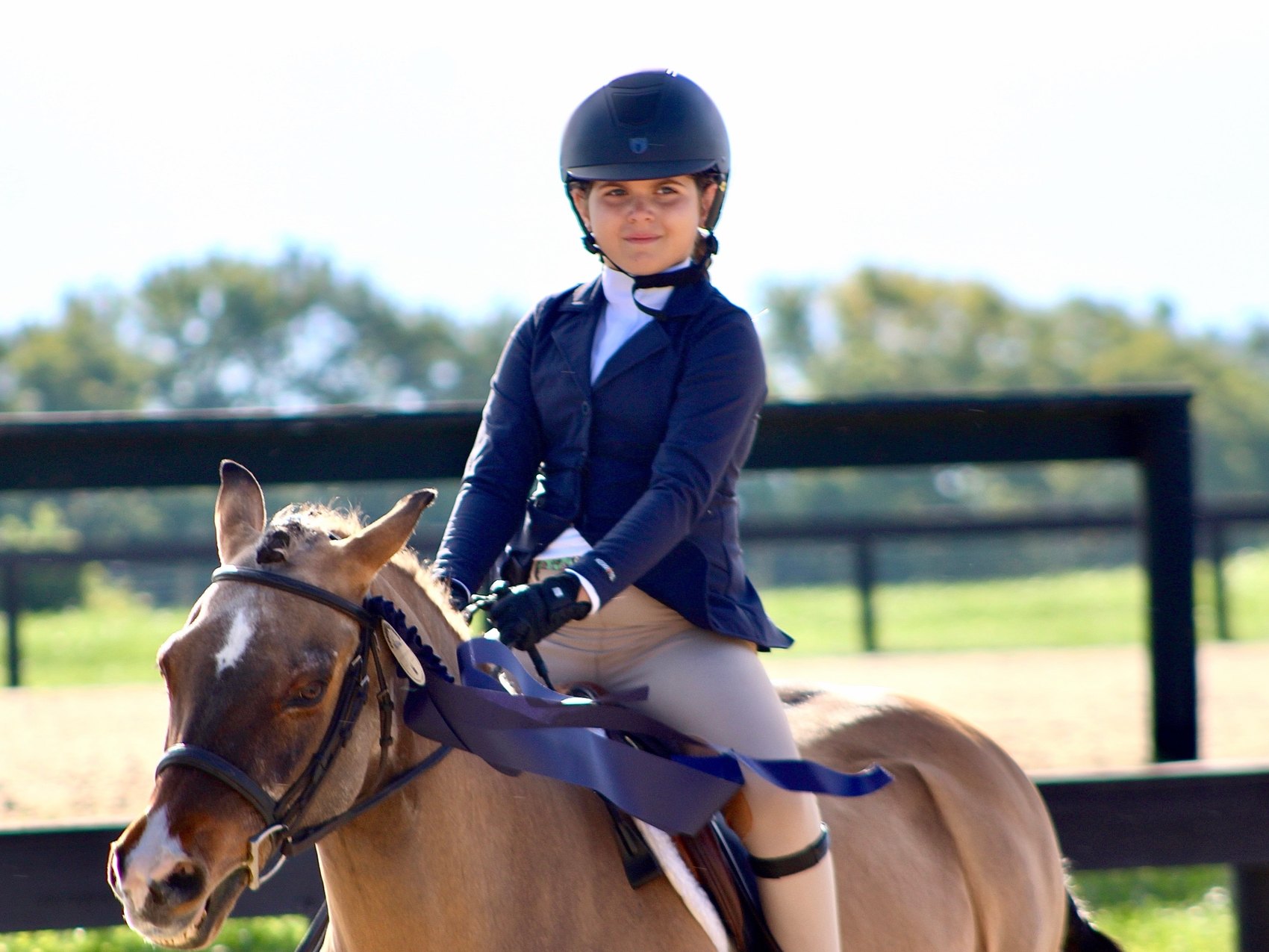 A junior rider on her pony with a ribbon after her class